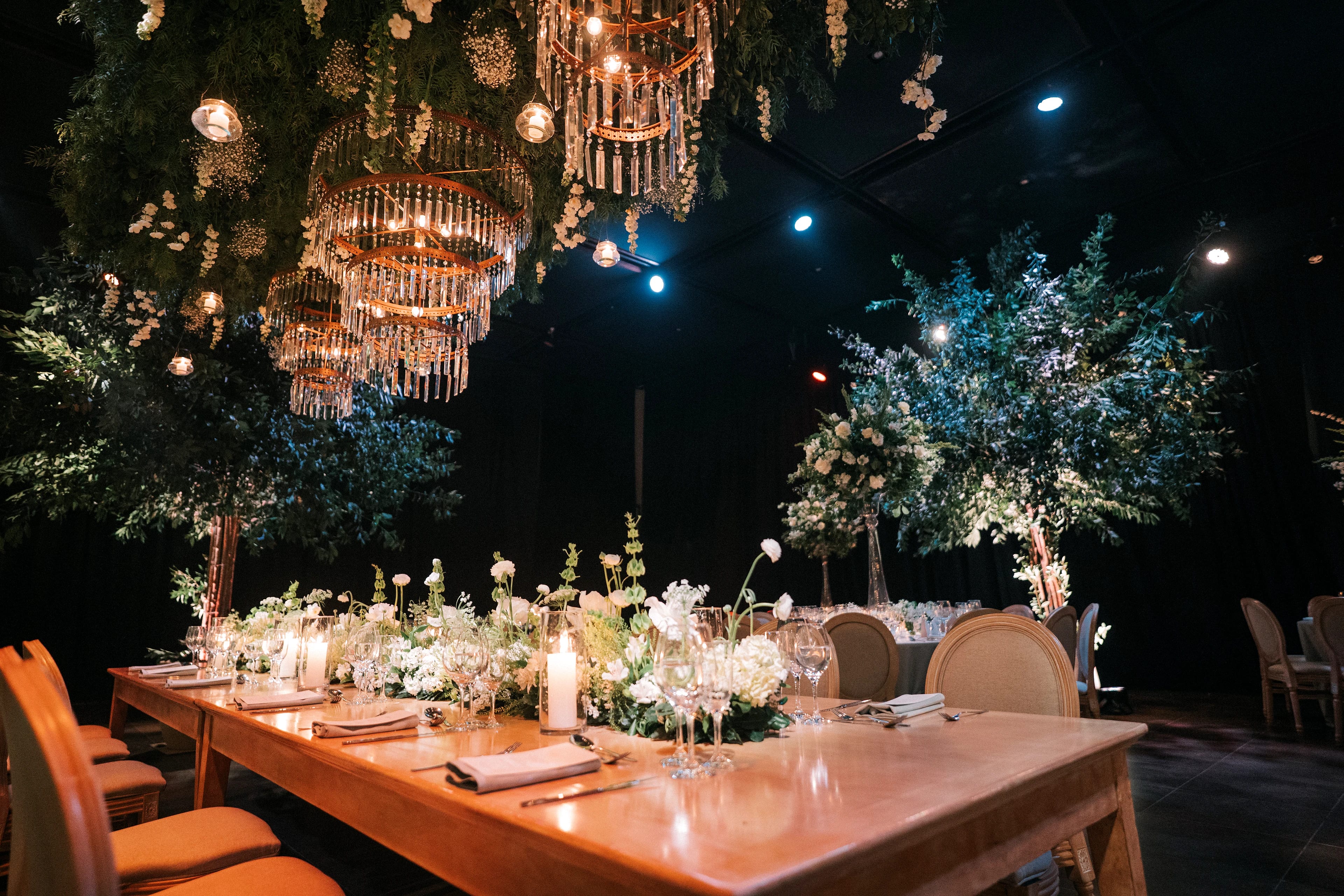 Mesa principal con flores blancas bajo arañas de cristal, en el salón de Rincón