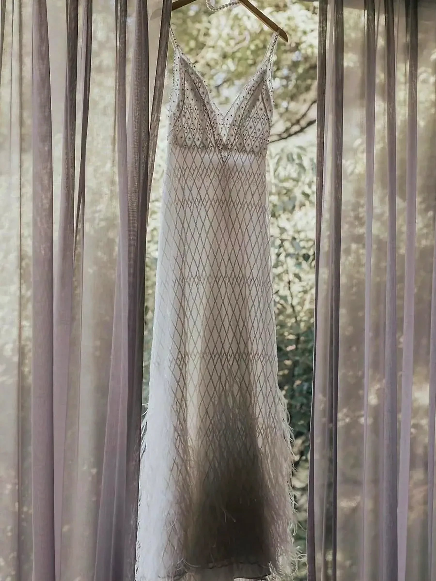 Vestido de novia colgado junto a la ventana, con el jardín de fondo