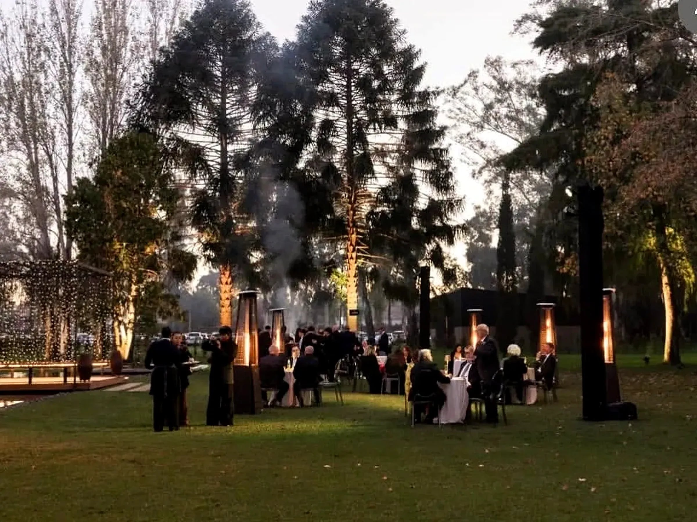 Invitados junto a las mesas altas del jardín de Rincón, al atardecer, junto a los calefactores