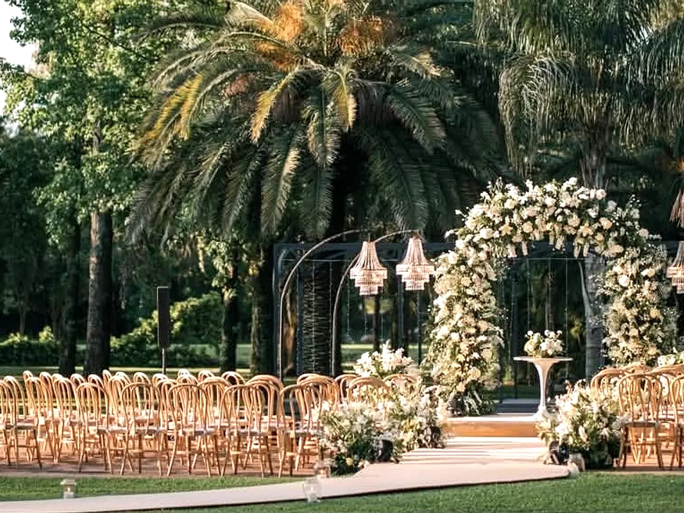 Pasillo de ceremonia con arco floral blanco y arañas colgantes, entre las palmeras de Rincón